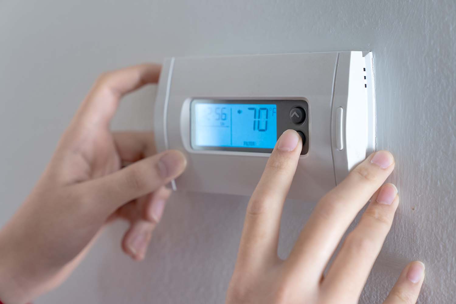 Hands adjusting temperature on a thermostat of a residential hvac system